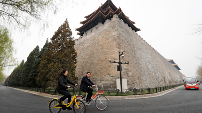 In this Wednesday, March 22, 2017 photo, people ride bicycles of bike-sharing companies Ofo, left, and Mobike, right, past a corner tower of the Forbidden City in Beijing, China. As many as 2.2 million of these two-wheelers have been deployed, which are available for rent for as little as U.S. 7 cents for half an hour, in the latest symbol of heavy spending in China's internet sector where startups are in a race to attract more users to their services.