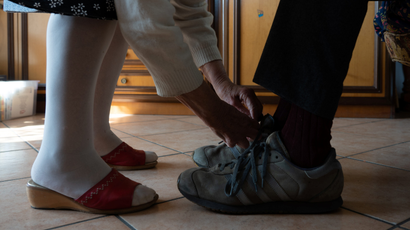A person in stockings is tying the shoes of a person wearing sneakers.