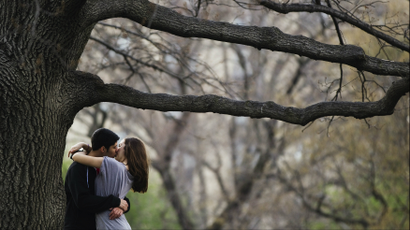 A couple kisses while standing underneath a tree inside Central Park during a warm day in New York.