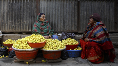 A woman chats with her friend as she waits for a customer while selling fresh lemons at the streets of Kathmandu