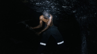 A bare-bodied man digs coal in a mine
