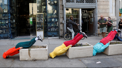 Three dancers face down on the pavement with their feet elevated on sidewalk planters in "Bodies in Urban Spaces" event 