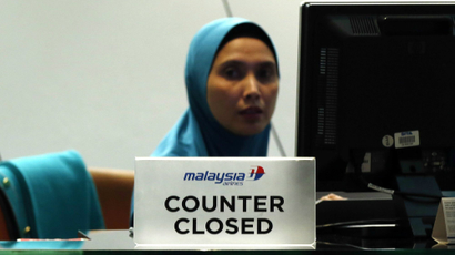 A staff member sits behind a closed Malaysia Airlines desk at Kuala Lumpur International Airport.