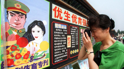 A visitor to a World Population Day exhibition in Beijing takes a photo of a propaganda billboard encouraging people to follow China's family planning policies, July 10, 1998. One slogan says, "One is too few, while two are just right."