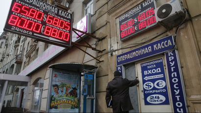 A man walks past a building and a board showing currency exchange rates in Moscow.