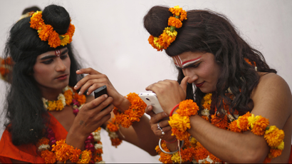 Two men dressed as Indian religious figures check their mobile phones.