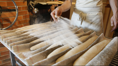 Baguettes in a bakery being sprinkled with flour.