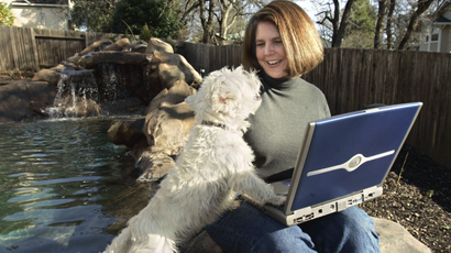 A woman looks at her dog, holds a laptop