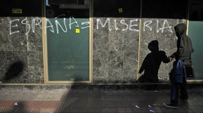 A man in front of graffiti on a building in Spain reading "España = Miseria"