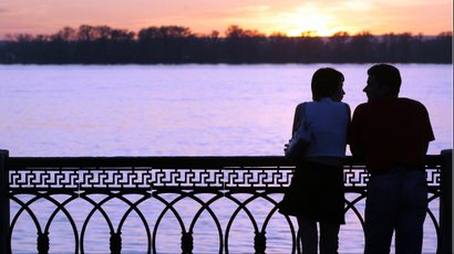 A couple stands close to one another on a bridge at sunset.