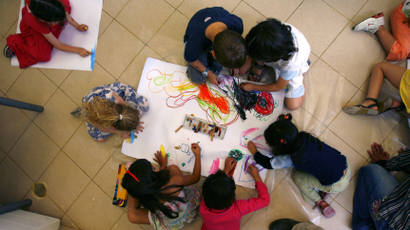 A group of preschoolers draws together on the ground.