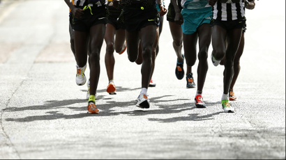 The legs of several runners against a white road