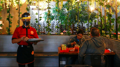 A waiter wearing a face shield and a protective mask carries a tray as he serves customers at a restaurant, as the Indonesian capital kicks off a two-week "transitional" period of eased restrictions, after the pace of coronavirus disease (COVID-19) infections slowed over the last two weeks, in Jakarta, Indonesia, October 12, 2020.