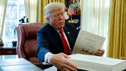 President Donald Trump grabs a box containing the tax bill after signing it in the Oval Office of the White House, Friday, Dec. 22, 2017, in Washington.