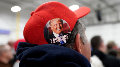A supporter wears a hat with a Trump button at a Trump rally