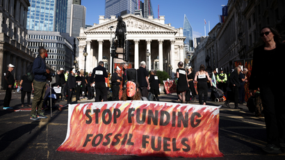 Climate activists protest outside the Bank of England with a sign saying "Stop funding fossil fuels."