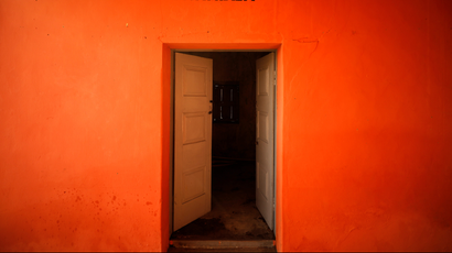An orange wall with a wooden door open leading into a separate chamber.
