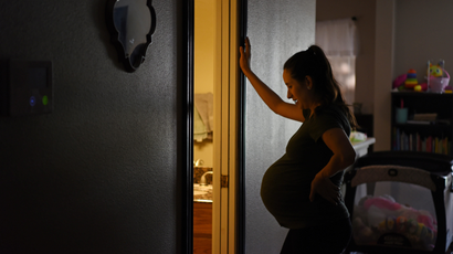 A pregnant woman leans against a door