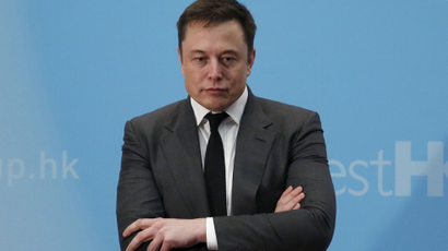 Elon Musk stands with his arms crossed