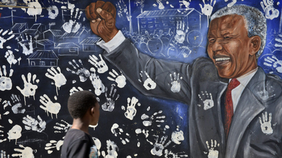 A boy stands before a mural of a smiling Nelson Mandela fist-pumping