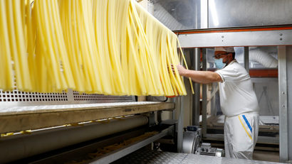 Worker with mask oversees pasta production.