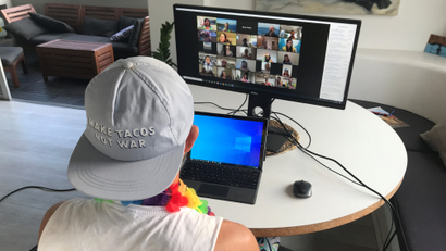 A man participates in a video call while wearing a backwards cap and a brightly colored lei.