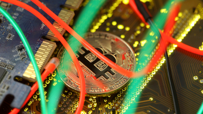 A gold coin emblazoned with the bitcoin symbol sits among wires and circuitboards.