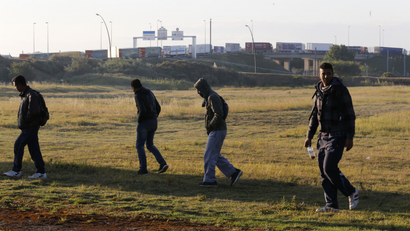 Migrants walk near the road after they left their hiding spot at the Eurotunnel site early in the morning as lorries queue to embark on shuttles at the Eurotunnel terminal in Calais, northern France, July 29, 2015.