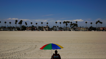 Angie Segi, 48, sits under an umbrella on the beach Friday, July 6, 2018, in Long Beach, Calif. Southern California sizzled Friday in record-breaking heat from the desert to the sea, with widespread triple-digit highs and withering conditions that stoked wildfires.