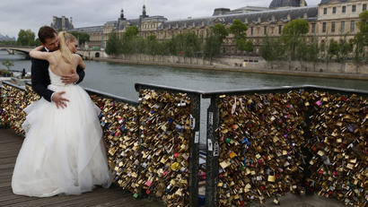 A recently-married couple embrace near grills covered with "love locks"