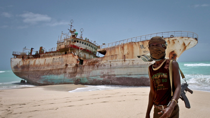 In this photo taken Sunday, Sept. 23, 2012, masked Somali pirate Abdi Ali stands near a Taiwanese fishing vessel that washed up on shore after the pirates were paid a ransom and released the crew, in the once-bustling pirate den of Hobyo, Somalia. The empty whisky bottles and overturned, sand-filled skiffs that litter this shoreline are signs that the heyday of Somali piracy may be over - most of the prostitutes are gone, the luxury cars repossessed, and pirates talk more about catching lobsters than seizing cargo ships.