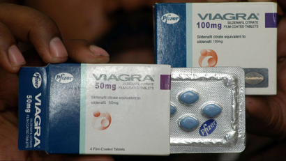 A hand holding a box of Viagra with some of the wrapped pills exposed.