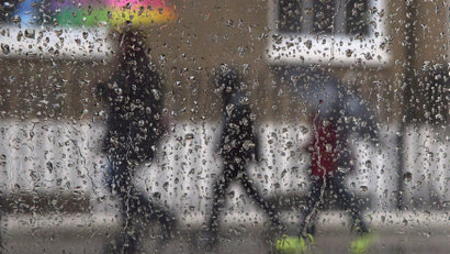 A family is seen through raindrops on a window as they shelter under umbrellas during a rainstorm