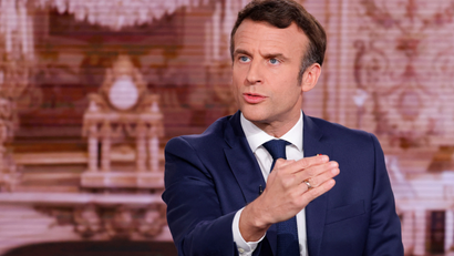 A close-up of French president Emmanuel Macron as he speaks with his hand raised.