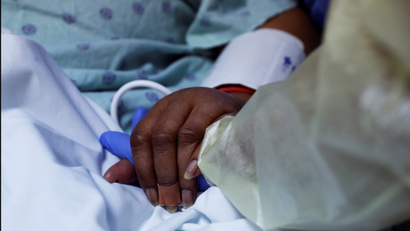 A healthcare worker holds hands with a person in a hospital bed.