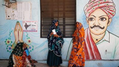 Women wait for a public transport outside a polling station after casting their votes at Sirohi