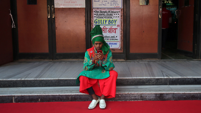 A man wearing traditional attire checks his mobile phone as he waits to perform before the launch of the trailer of a Bollywood movie outside a cinema in Mumbai