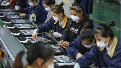 Employees, wearing masks, work on a production line manufacturing display monitors at a TPV factory in Wuhan