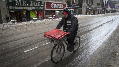 A pizza delivery man rides on a bicycle on 8th avenue in New York city.