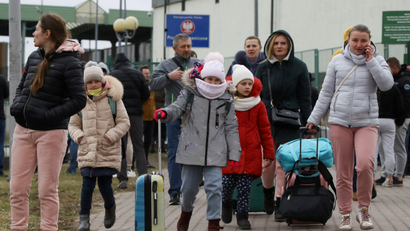 Ukrainians dressed in coats and hats, carrying suitcases, arrive at the border with Poland.