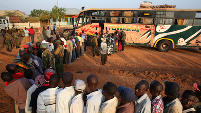 Passengers travelling to Nairobi stand in front of a bus, as they wait to be searched for weapons by Kenyan police, in the town of Mandera at the Kenya-Somalia border December 8, 2014.
