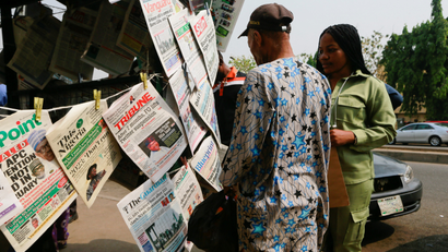 A man and a lady glancing at the pages of newspapers at a newspaper stand