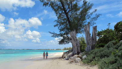 People walk on a glistening beach in the Cayman Islands, which have promised to open up their books.