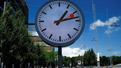 People walk past a giant replica of a station clock at a Swiss Rail company (SBB) administrative building in Bern