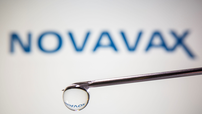 A stock image of a syringe with a drop of liquid coming out in front of the Novavax logo