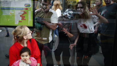 A woman and a child wait for a bus as actors dressed as zombies gesture for attention during a zombie walk in Belgrade.