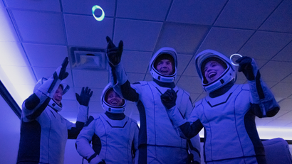 Four space tourists wear spacesuits and juggle glow rings.