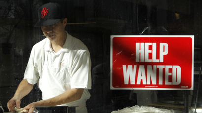 A man prepares a meal near a help wanted sign hanging in a restaurant window in San Francisco,