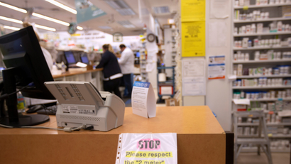 The counter in a pharmacy line. Drugs are visible on the right hand side, and a sign by the register reminds patients to wait six feet behind each other.