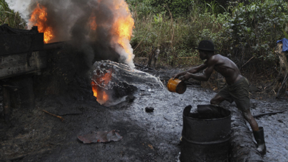 A man pours water over a fire at some stage during an illegal oil refining process